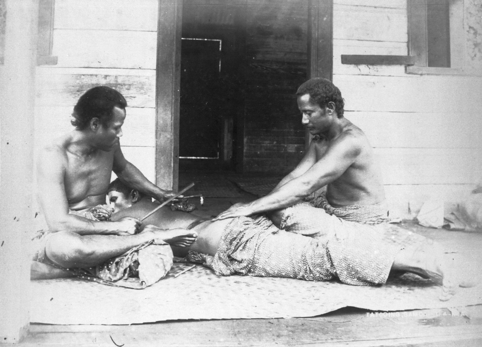 A Samoan tattooist (left), Tufuga ta tatau and assistant (right), carrying out a traditional tatau on a man's back. The tattooist uses traditional tools (1895) photographed by Thomas Andrew (1855-1939) via Wikimedia Commons